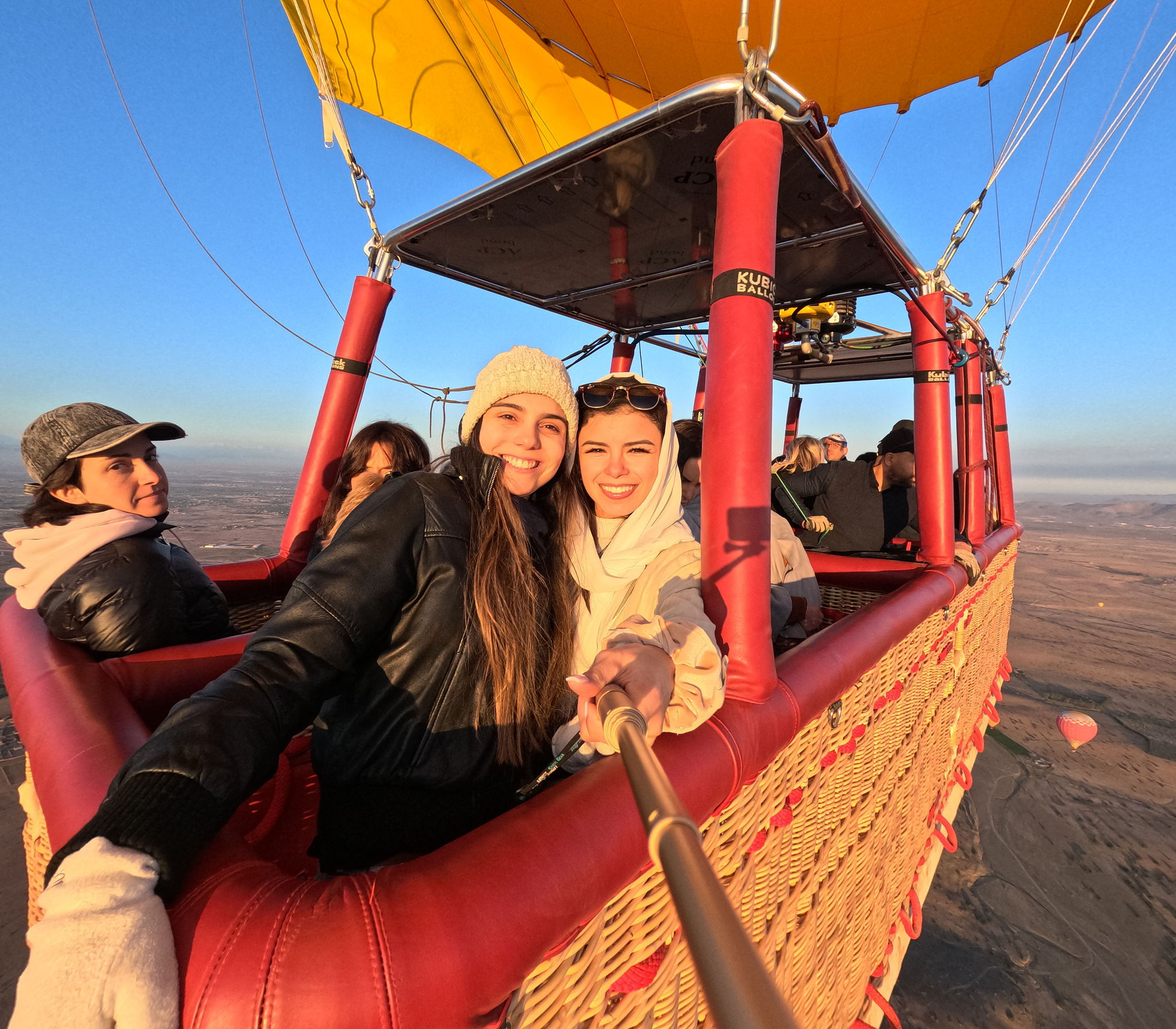Two guests in a yellow balloon basket over the Marrakech plain, another balloon in the distance