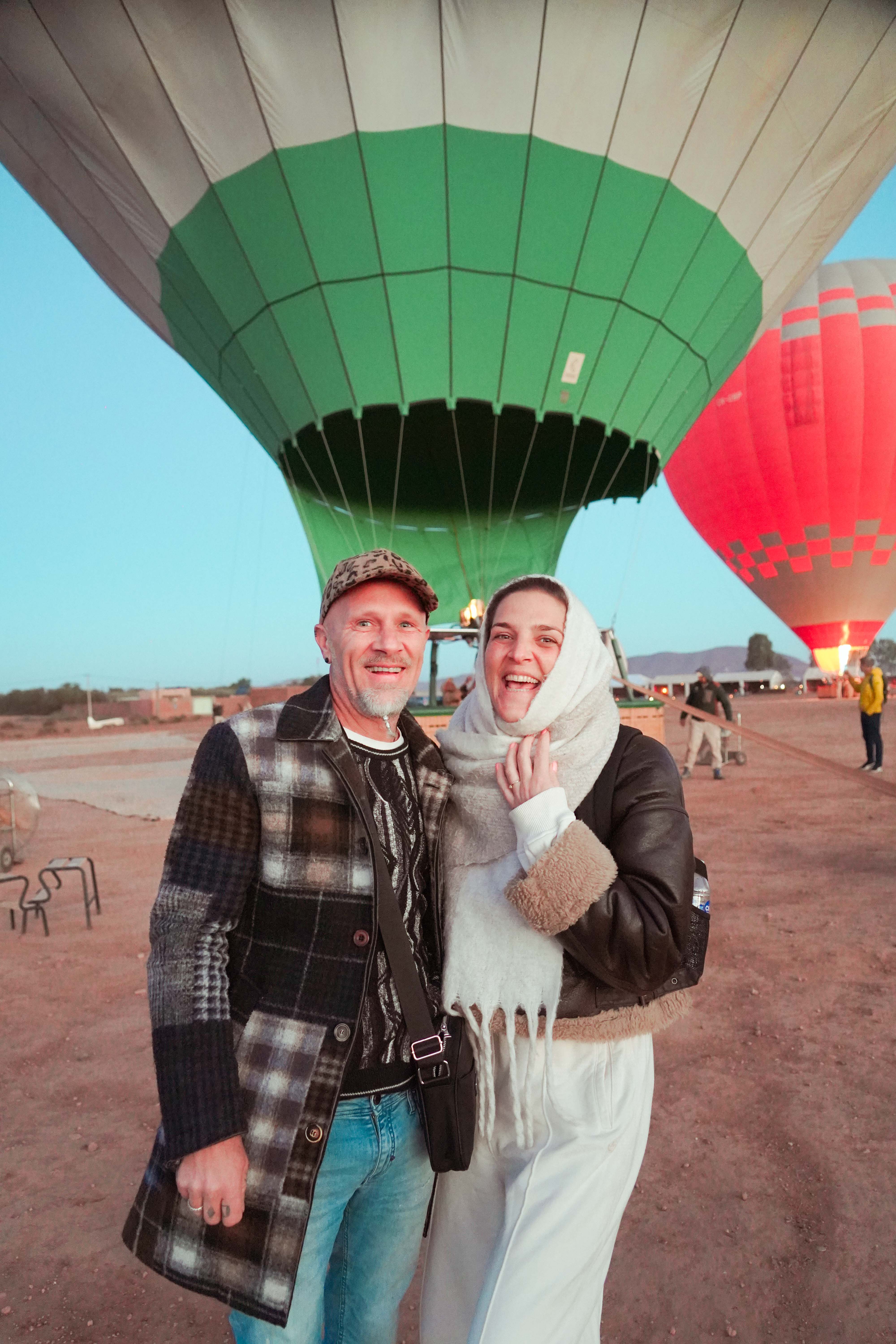 Two guests at the launch field at dawn, balloons inflating behind them