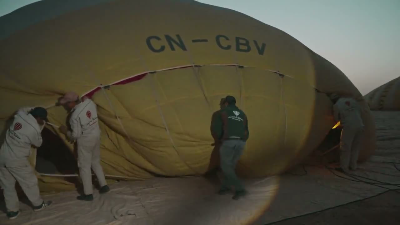 Ground crew inflating a yellow envelope before sunrise, burner firing