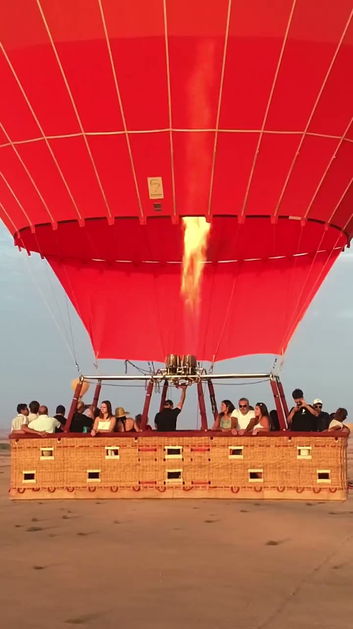Passengers in a packed red balloon basket as the burner fires at sunrise