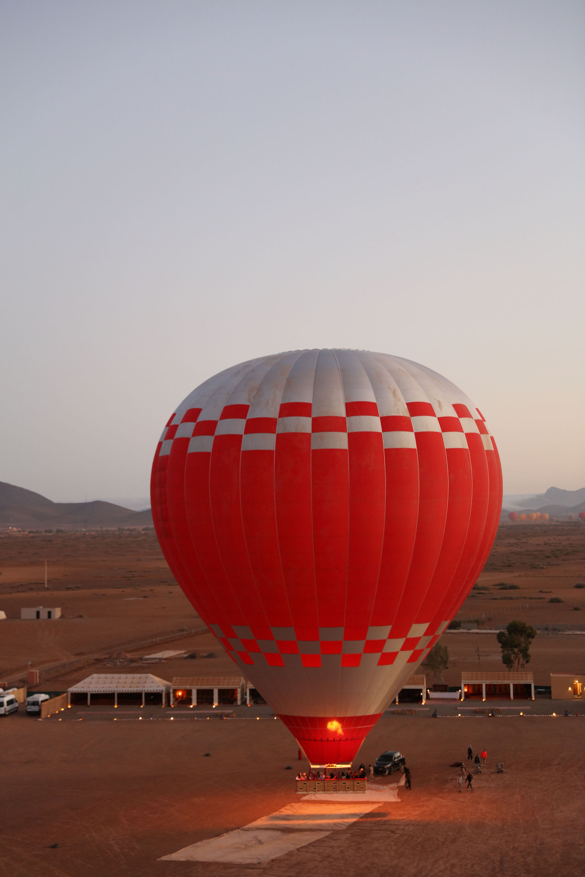 A red balloon standing on the launch field at dawn, burner glowing in the throat